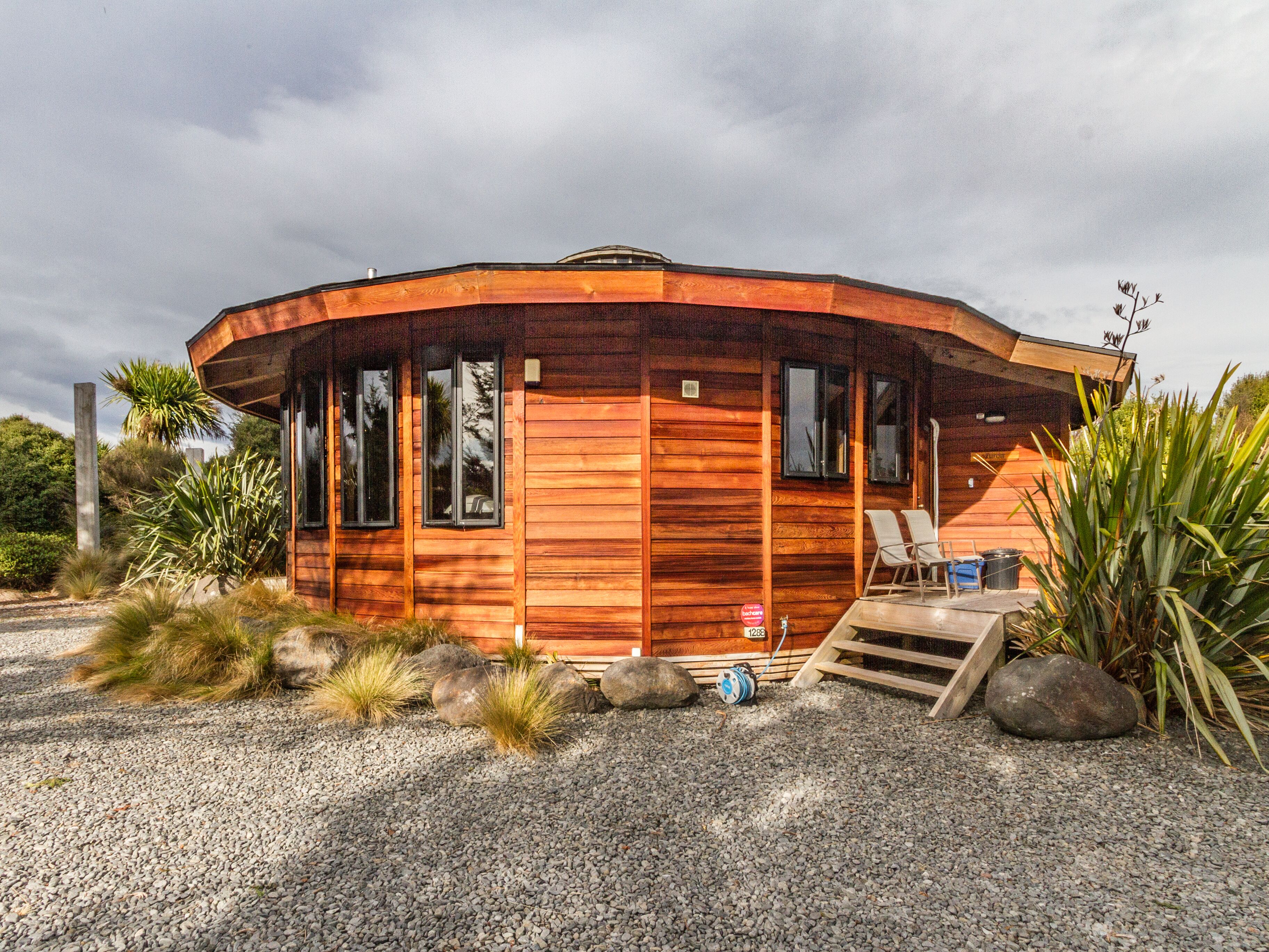 A wooden cabin with a curved roof, large windows, and a gravel driveway.