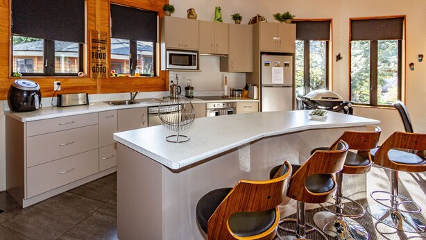 Une cuisine moderne avec des meubles en bois, un îlot central doté de tabourets, un four à micro-ondes et un réfrigérateur.
