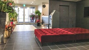 A modern lobby with a red sofa, tiled flooring, and potted plants.