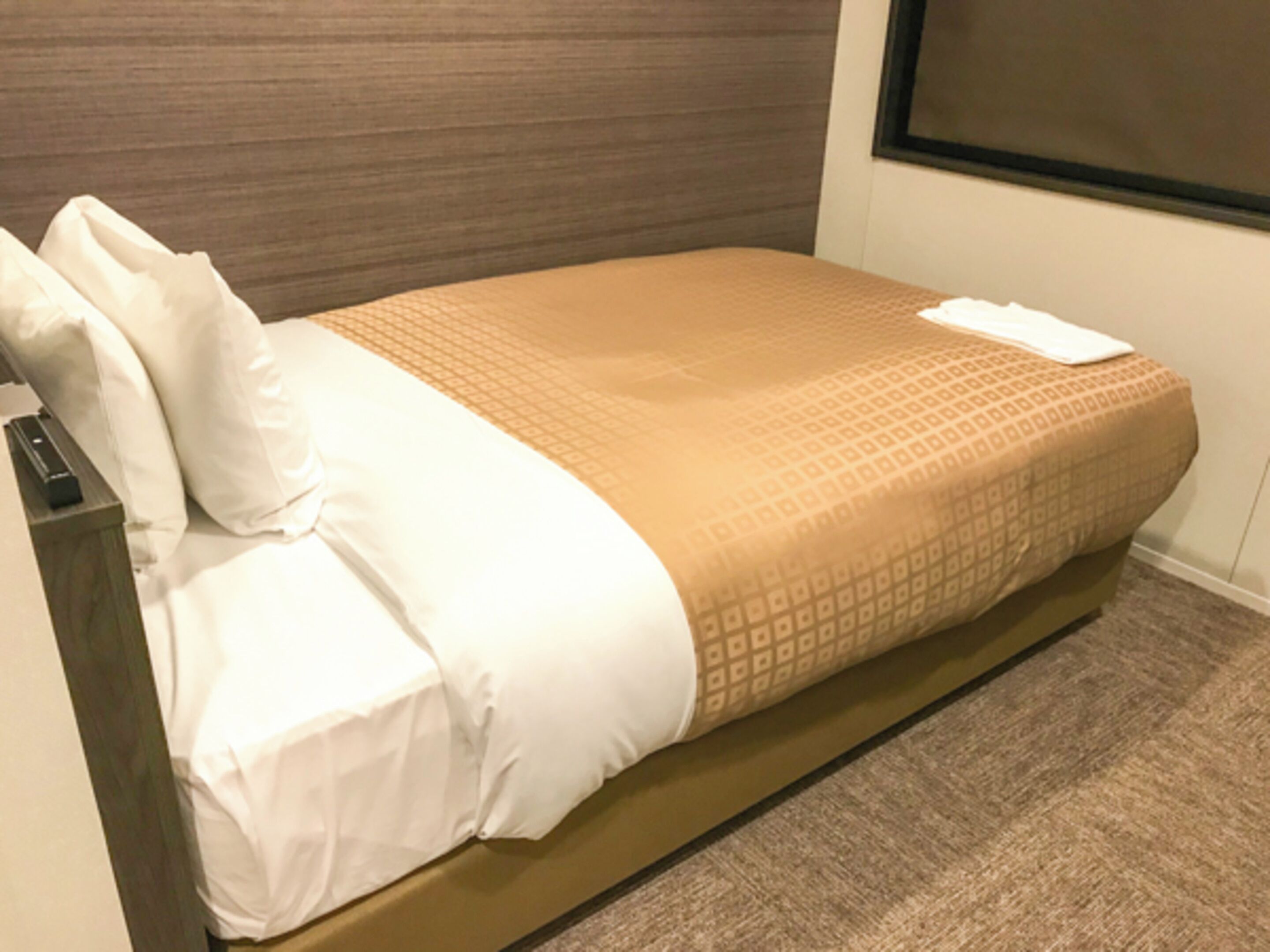 Una cama bien hecha con una colcha estampada y almohadas, un cabecero de madera y piso alfombrado.