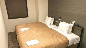 A double bed with a beige bedspread and white pillows, a wooden headboard, and a small bedside table with a lamp.