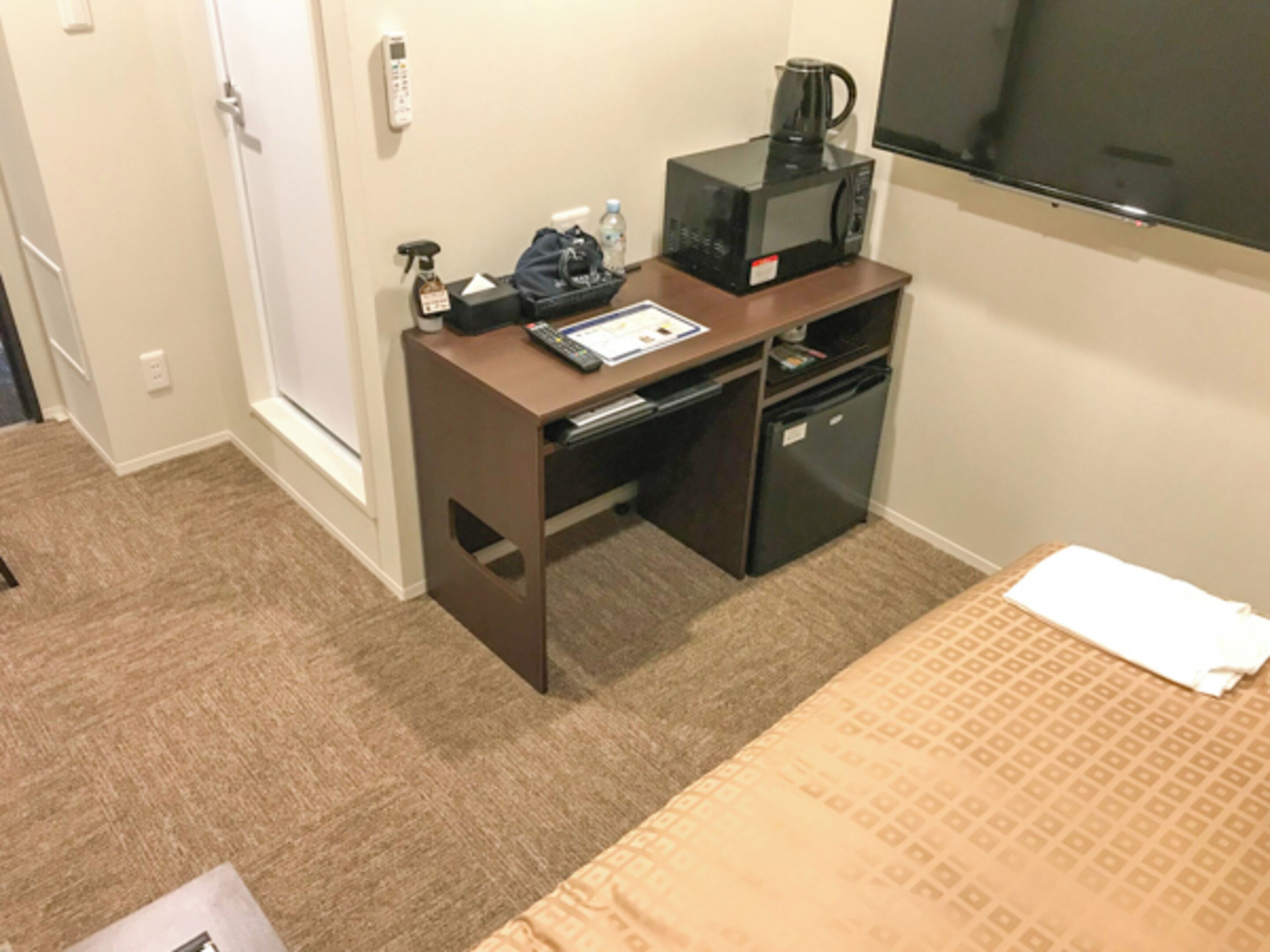 A compact hotel room with a bed, a desk with a microwave, a coffee maker, and a TV.