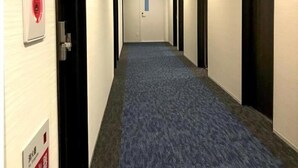 A hotel hallway with carpeted floors, doors on both sides, and a light fixture on the ceiling.