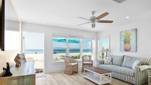 Una habitación luminosa con vistas a la playa, sillones de mimbre, un sofá a rayas y un ventilador de techo.