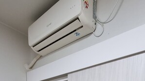 Una habitación con un equipo de aire acondicionado blanco, una puerta corredera y un pequeño espacio de almacenamiento con pantuflas.