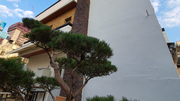 Un edificio con un letrero rojo llamativo que dice "DAEGU HOUSE" y una pared blanca grande.
