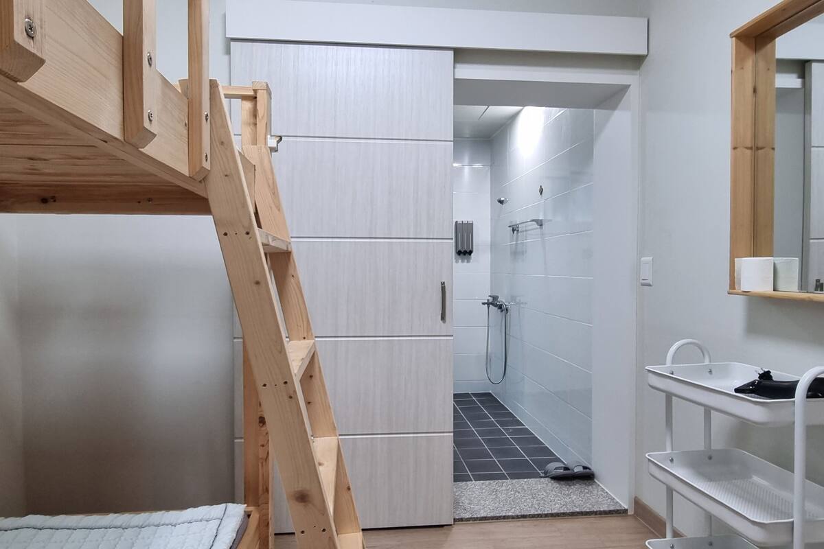 A compact room with a wooden bunk bed, a small bathroom with a shower, and a white sink with a mirror.