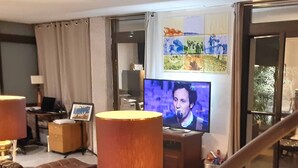 A living room with a sofa, two lamps, a television, and a wall with pictures. - Duplex garden terrace in the heart of Juan-les-Pins. 6/8 people. (Antibes)