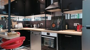 A modern kitchen with black cabinets, a wooden countertop, and stainless steel appliances including a dishwasher, oven, and microwave. - Duplex garden terrace in the heart of Juan-les-Pins. 6/8 people. (Antibes)
