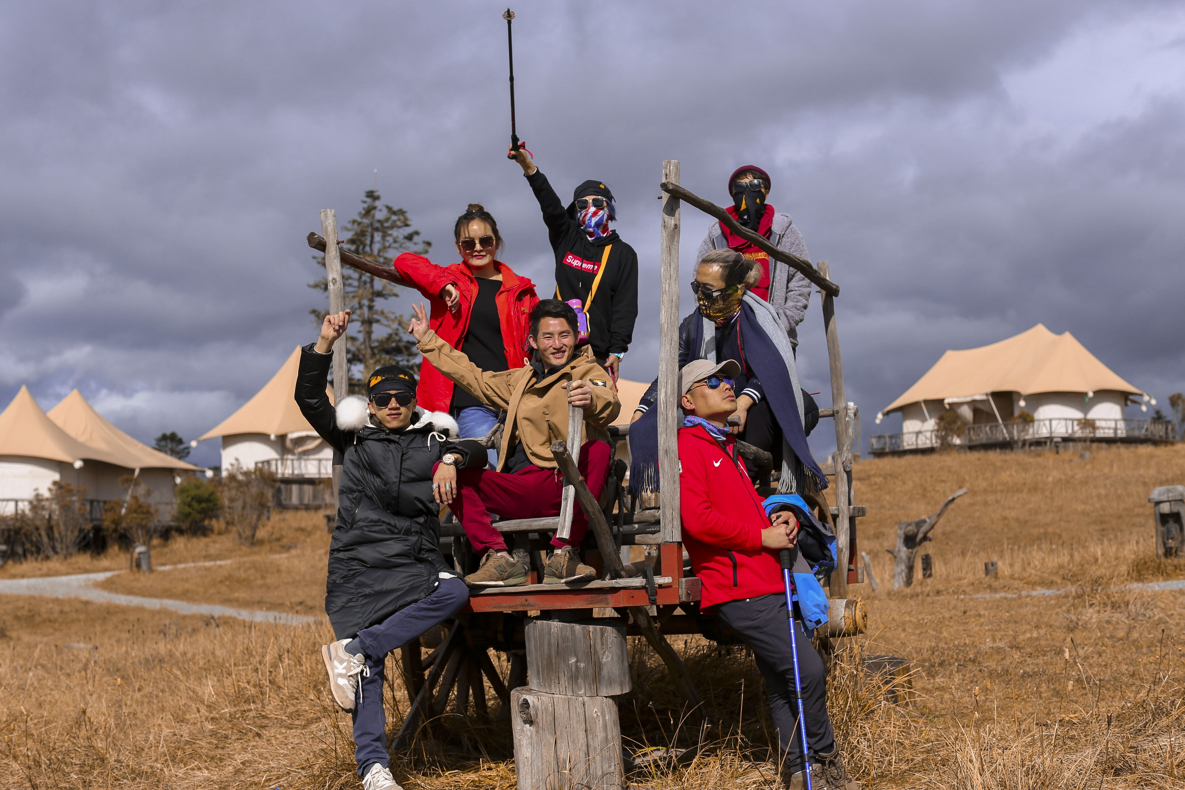 A group of people on a wooden structure in an outdoor setting with tents in the background.
