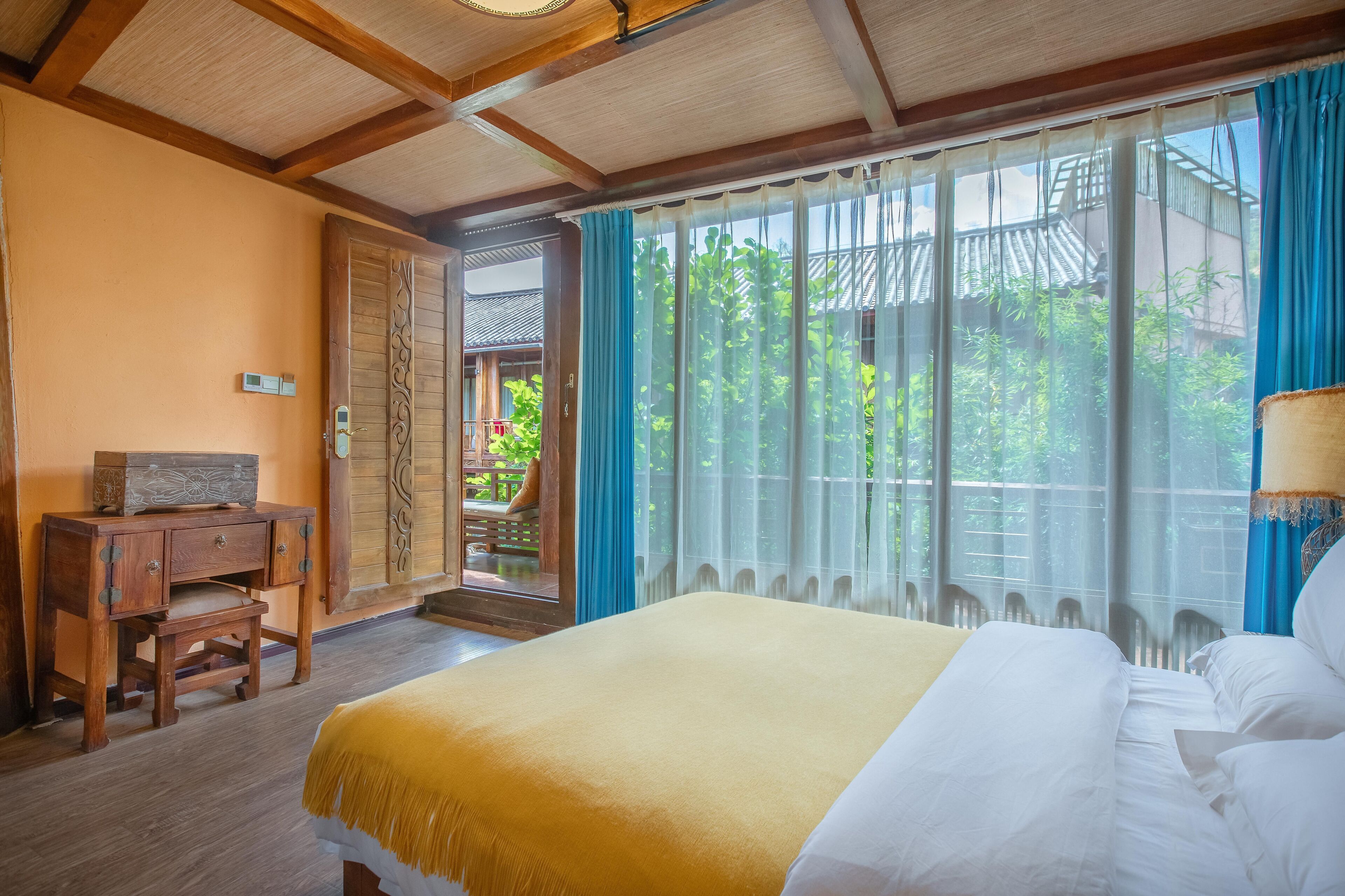 Quarto de hotel com cama, escrivaninha de madeira e vista para o verde lá fora.