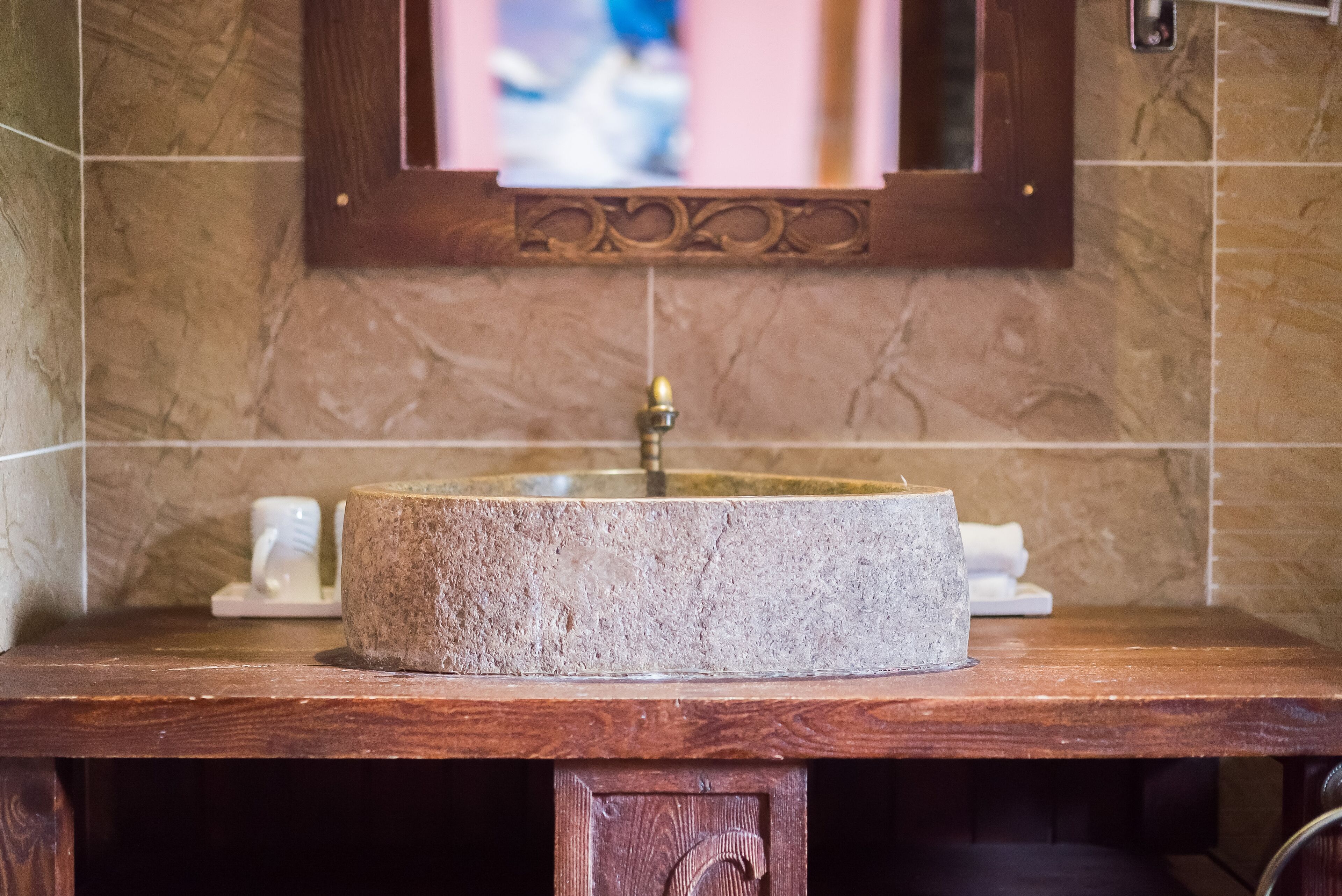 A bathroom with a round stone sink, wooden countertop, and a mirror with a decorative frame.