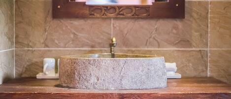 A bathroom with a round stone sink, wooden countertop, and a mirror with a decorative frame.