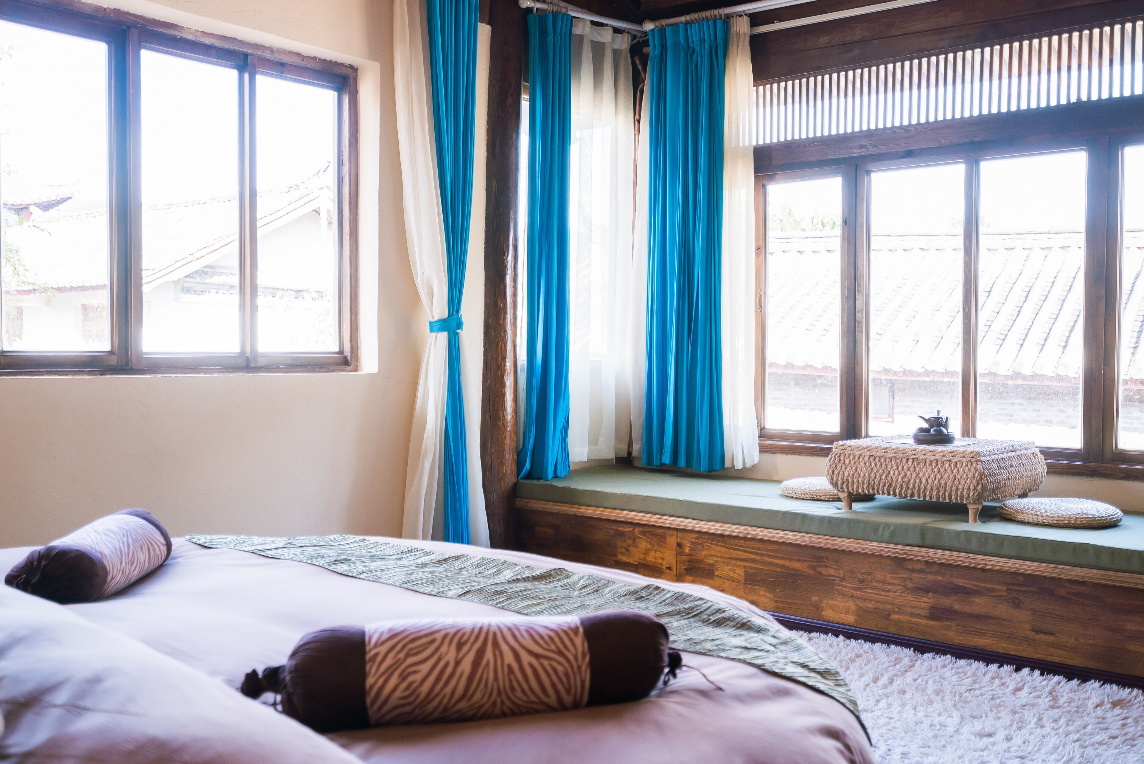 A bedroom with a large bed, a window seat with cushions, and curtains.
