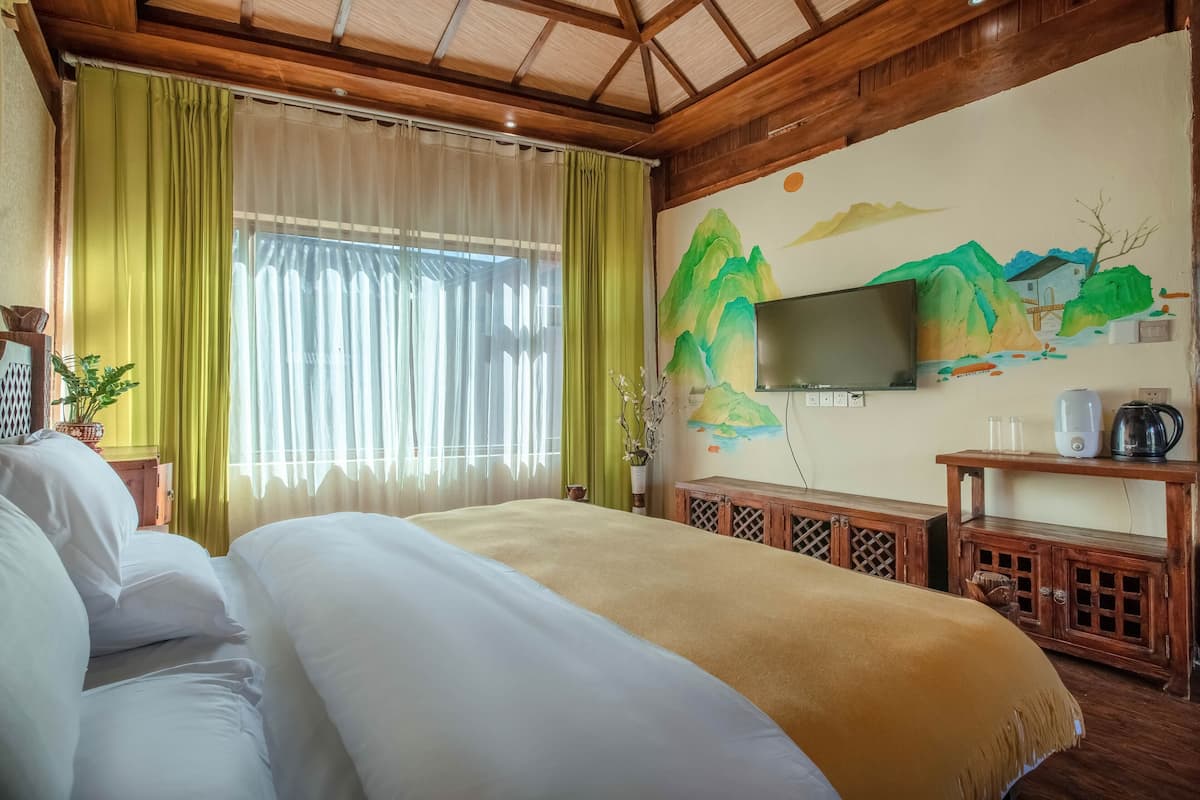 Ein Hotelzimmer mit einem großen Bett, einem an der Wand befestigten Fernseher, einem Holzschrank und einem Bergpanorama.
