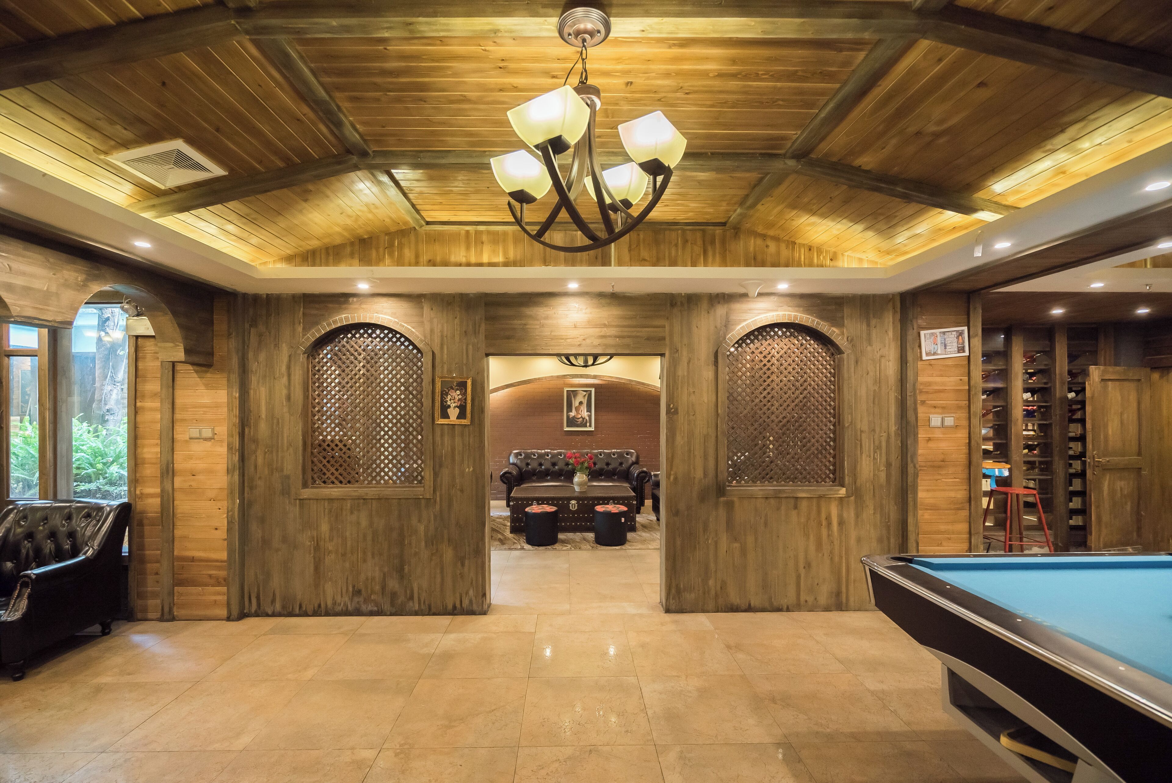 A pool table, wooden walls, a chandelier, and a sofa in a room with a wooden ceiling.