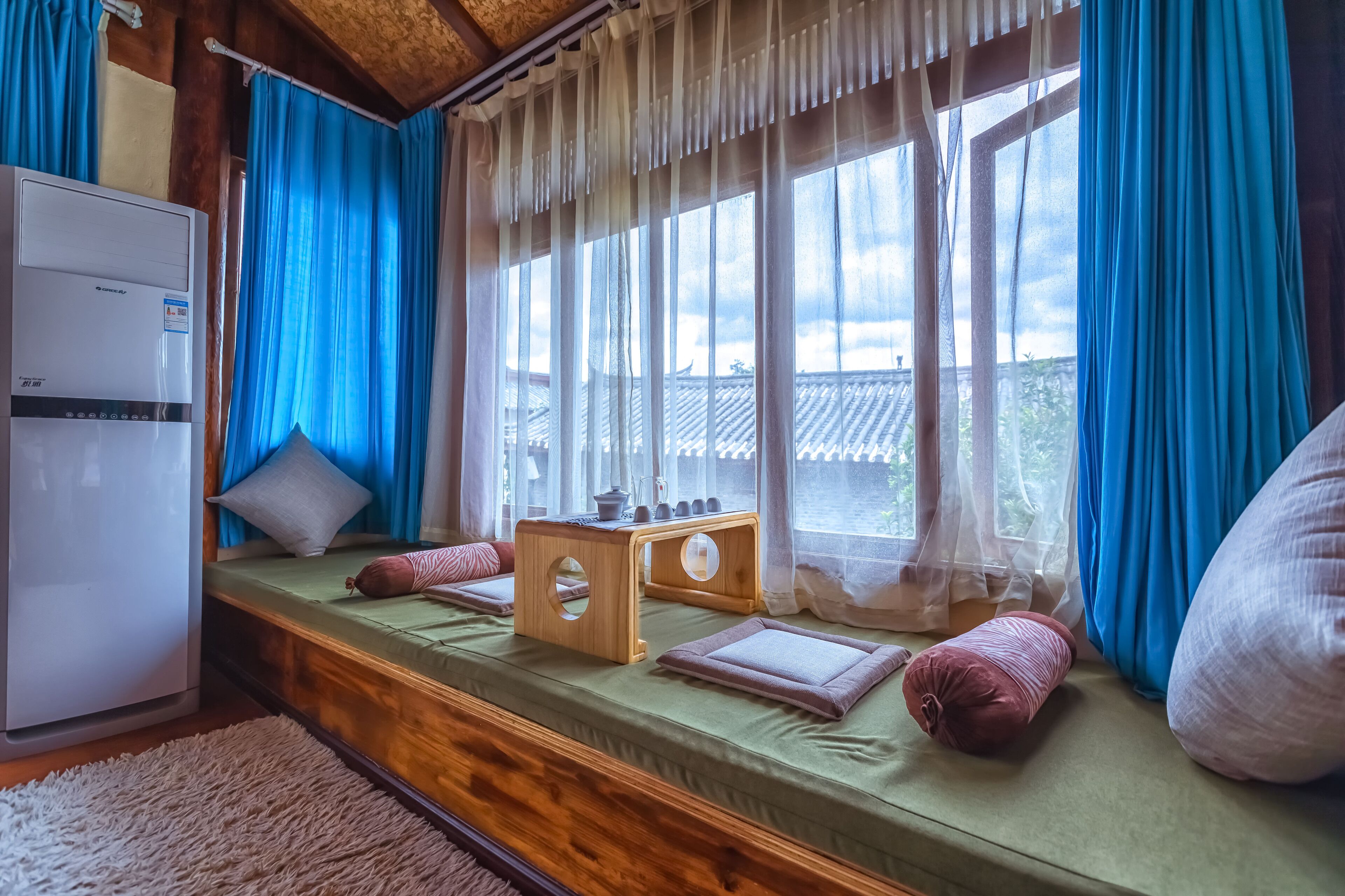 A room with a bed, a small wooden table, and a window with curtains.