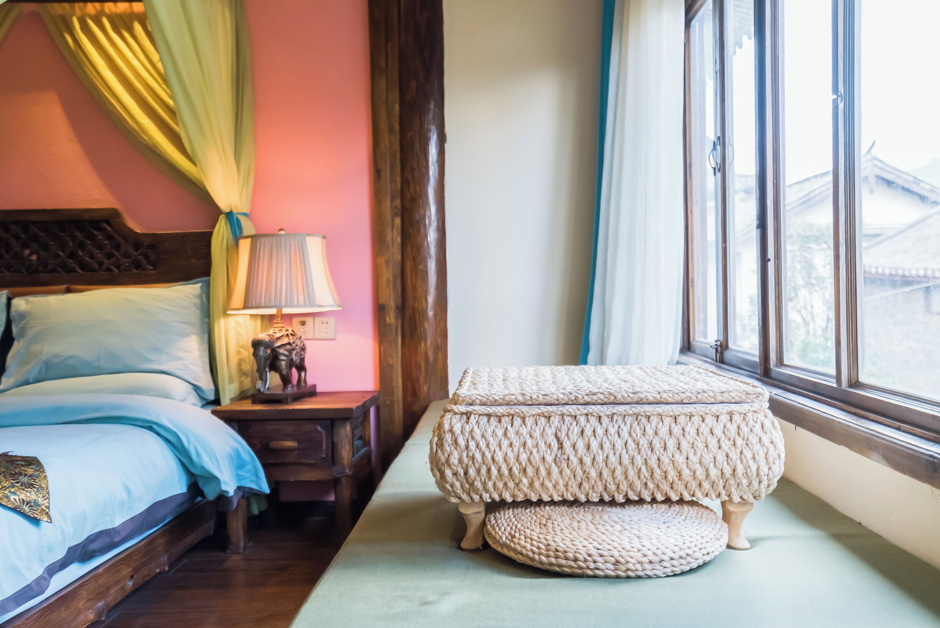 A bedroom with a bed, bedside table, lamp, and window with curtains.