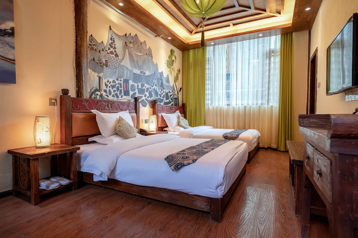 Ein Hotelzimmer mit zwei Betten, Holz-Kopfteilen, einem Wandbild, einer Holzkommode und einem Nachttisch mit Lampe.