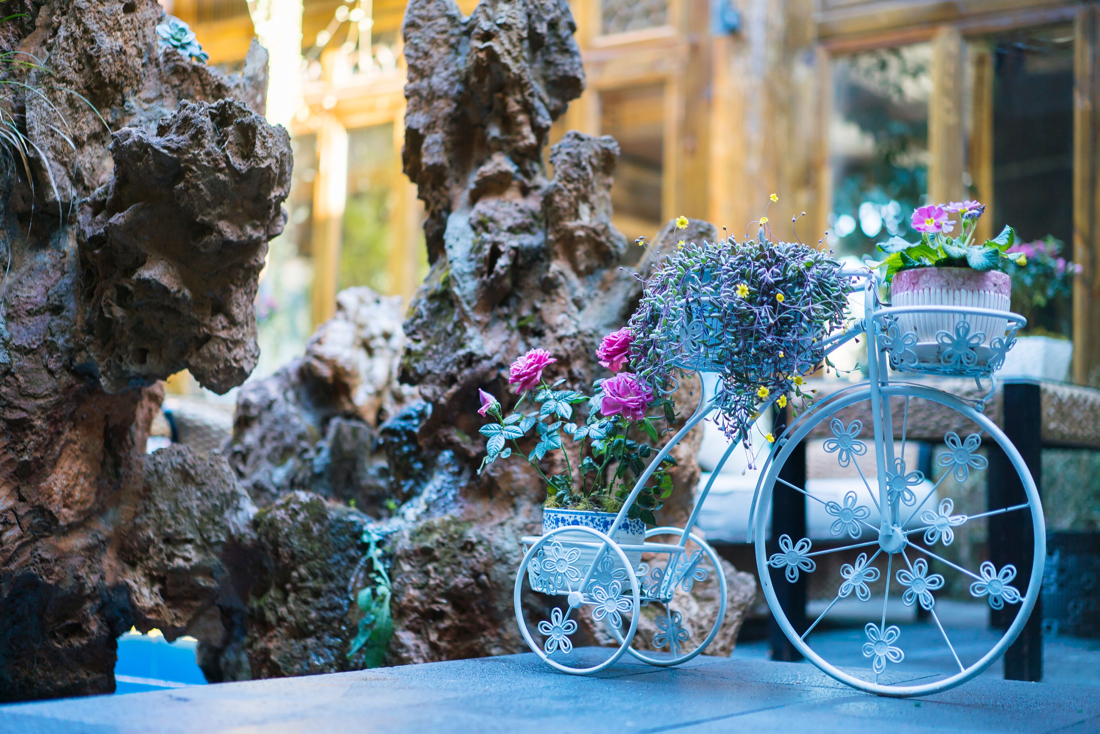 Una bicicletta in metallo con decorazioni floreali e un cesto, appoggiata su uno sfondo roccioso.