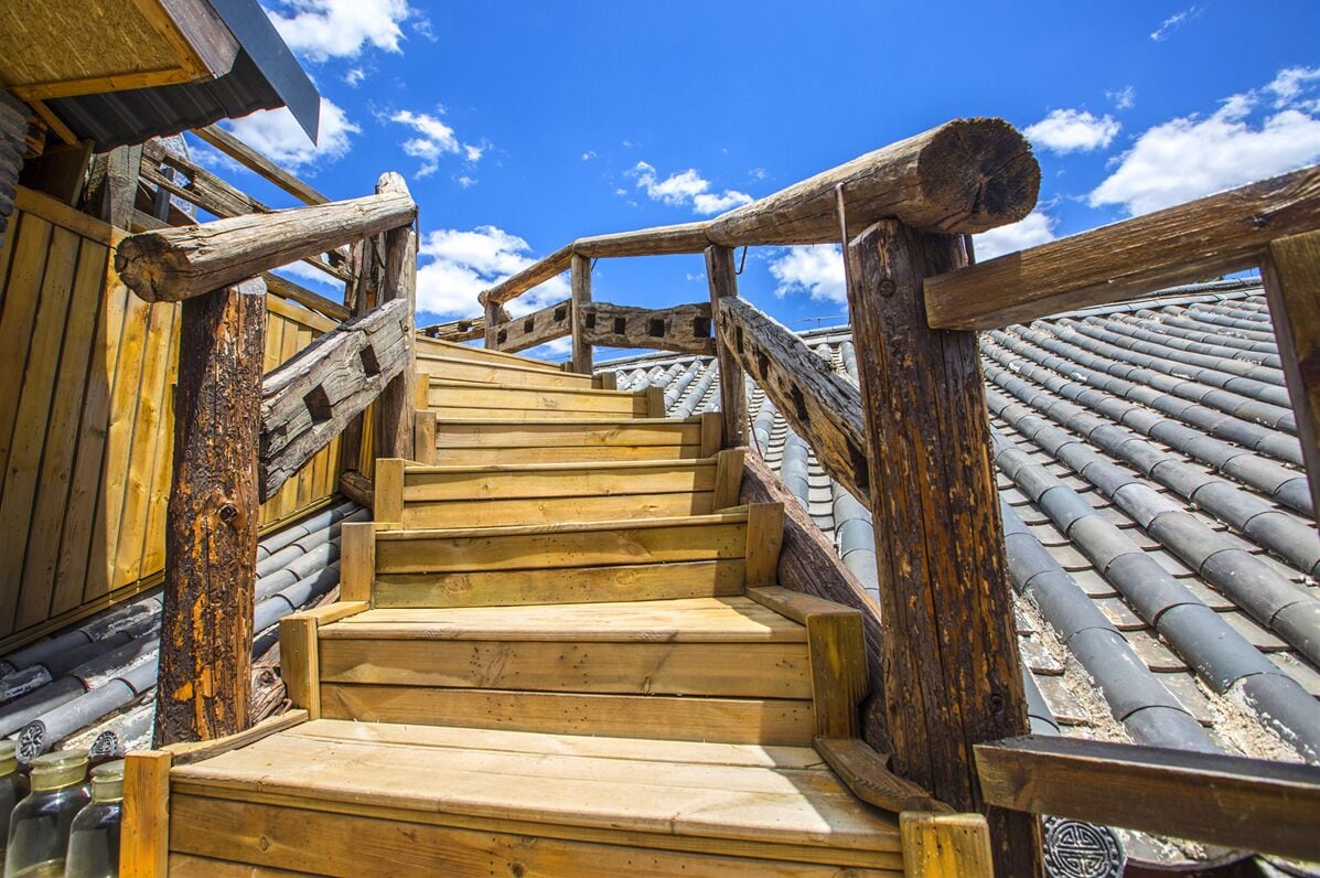 A wooden staircase with a traditional design, leading to a building with a tiled roof.