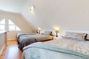 A bedroom with three beds, wooden flooring, and a sloped ceiling with skylights.
