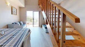 Ein geräumiges Schlafzimmer mit einer Holztreppe, einem Bett mit gestreifter Bettwäsche, einer Sitzecke mit Kissen und einem großen Fenster, das für natürliches Licht sorgt.