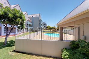 A residential building with a swimming pool, surrounded by a fence and greenery.
