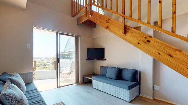 Ein modernes Wohnzimmer mit einer Holztreppe, einer Couch, einem Fernseher und einem Balkon mit Blick.