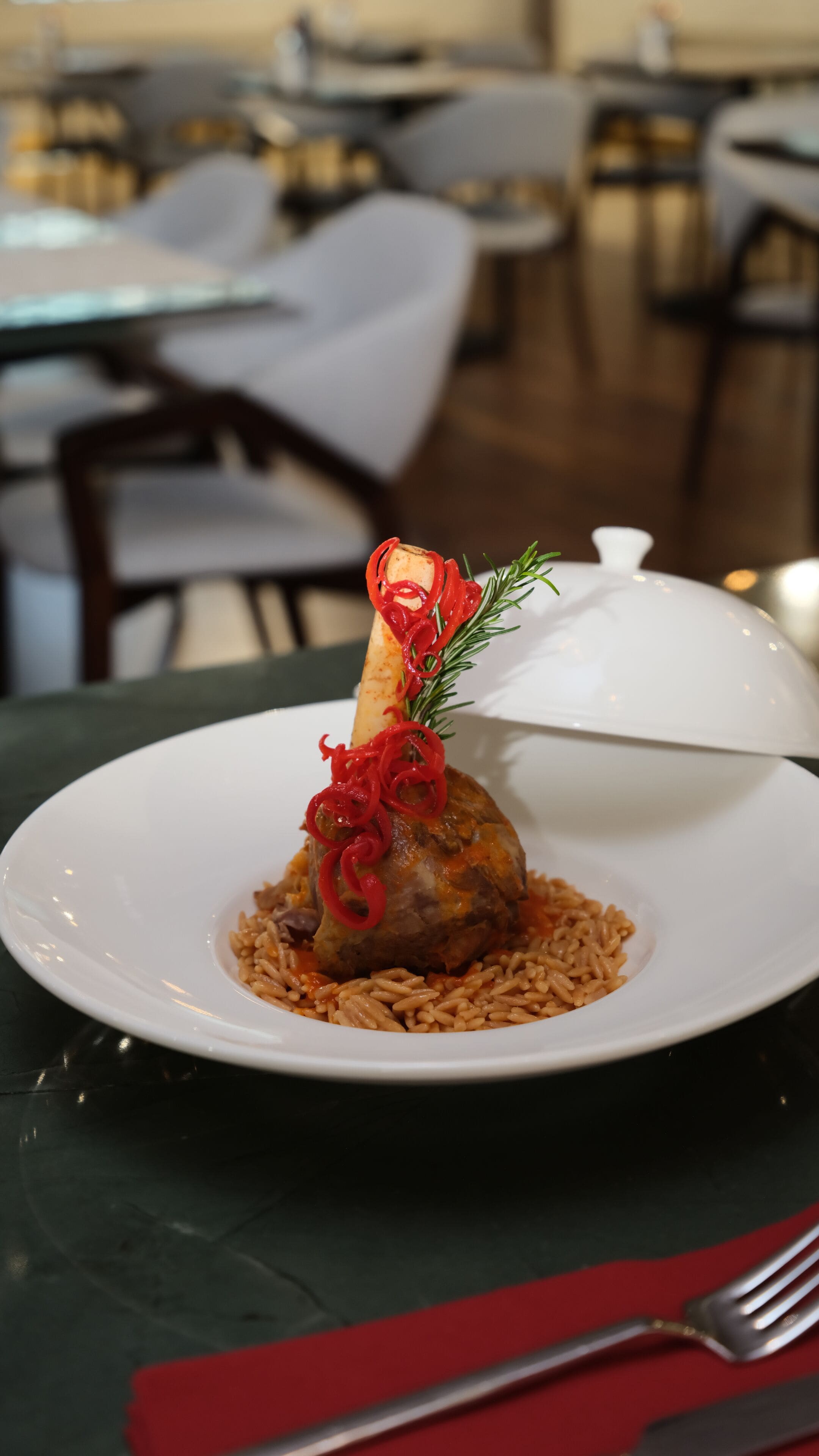 A plate with a meat dish, garnished with red spirals and a sprig of rosemary, on a white plate.