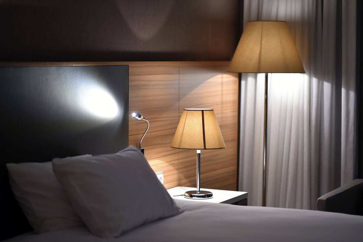 A hotel room with a bed, a nightstand, a lamp, and a window with curtains.