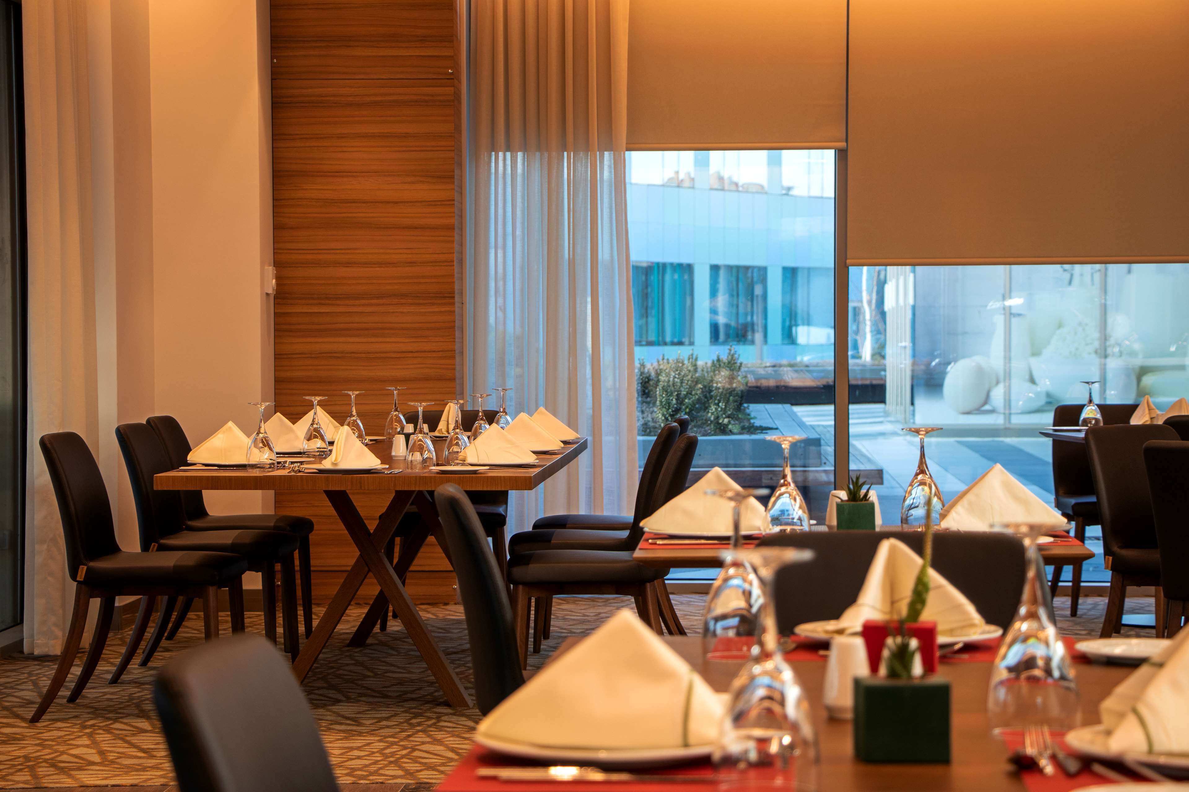 A dining area with a table set for six, chairs, and a view of a building through large windows.