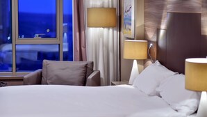Habitación de hotel con una cama grande, dos mesitas de noche, una ventana con cortinas y un televisor de pared.