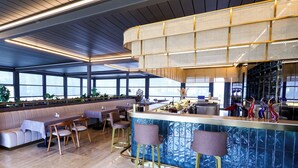 Un restaurante moderno con zona de bar, mesas y vistas amplias a través de grandes ventanales.