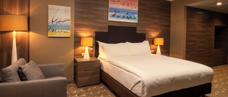 A hotel room with a large bed, two bedside tables with lamps, a sofa, and artwork on the walls.