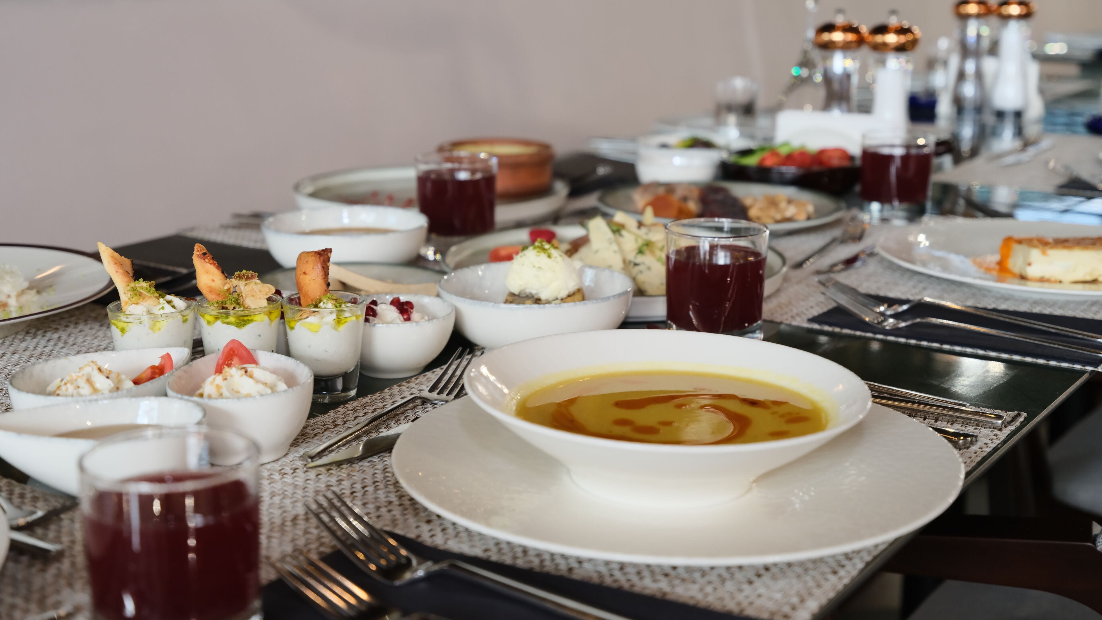 A dining table with various dishes, including bowls of soup and desserts, and glasses of red beverage.