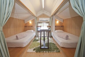 A compact, well-lit room with two single beds, a small table, and a window providing natural light.