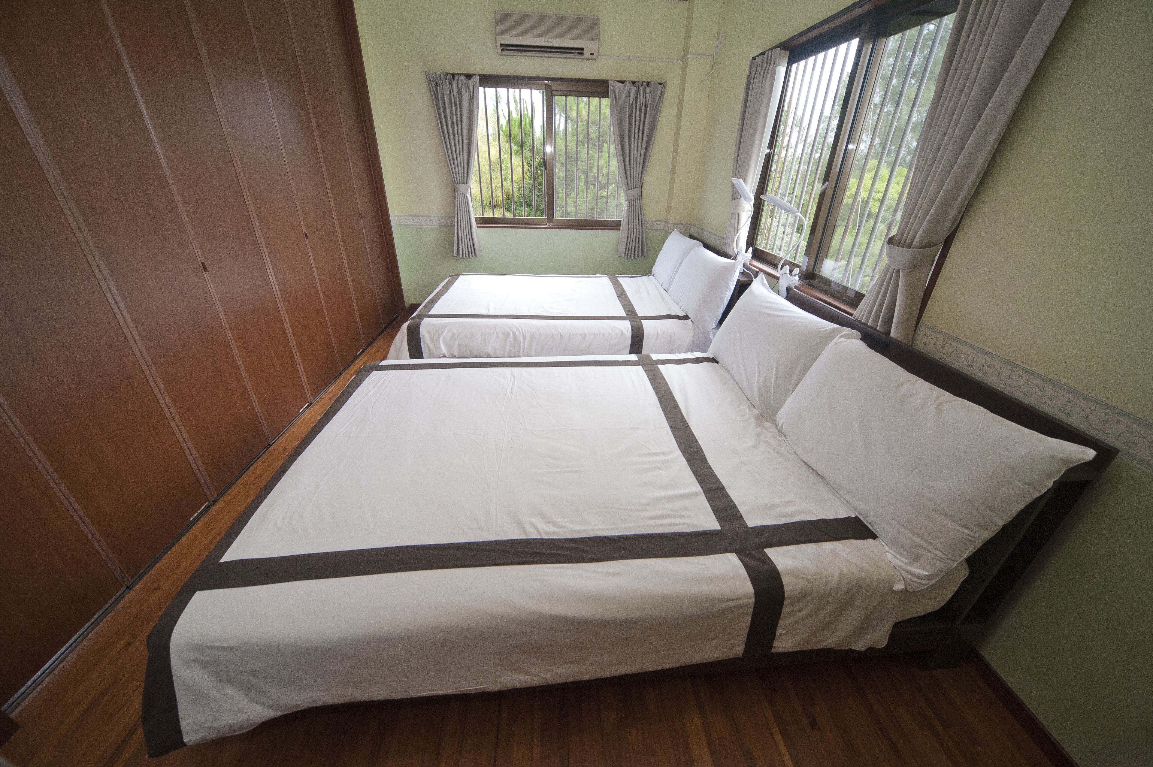 A room with two beds, wooden paneling on the walls, and a window with curtains.