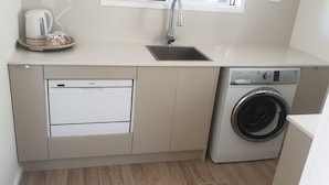 Cocina compacta con lavavajillas, lavadora, pileta y tetera sobre la encimera.