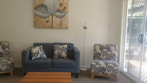 Una sala de estar con un sofá gris, dos sillones estampados, una mesa de centro de madera y una lámpara de pie.
