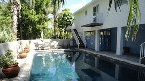Une piscine à l’eau d’un bleu limpide, entourée de plantes en pot et de mobilier d’extérieur.