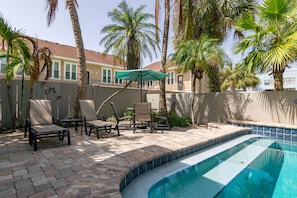 Un patio trasero con piscina, muebles de jardín y palmeras.