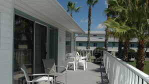 Un balcon avec des chaises blanches et une table, des palmiers et un bâtiment avec un toit bleu.