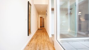 Un pasillo moderno con piso de madera, paredes blancas y una puerta de cristal que da a una habitación.