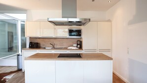 Una cocina moderna con armarios blancos, una campana extractora de acero inoxidable, un horno y una cafetera.