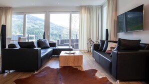 Una sala de estar moderna con dos sofás negros, una mesa de centro de madera y un amplio ventanal con vistas a las montañas.