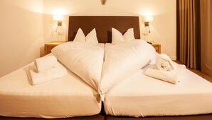 Cama doble con dos almohadas y dos toallas, cabecera de madera, lámparas de noche y apliques de pared.