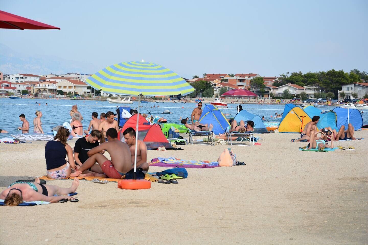 A beach with people sunbathing, tents, and a striped umbrella.