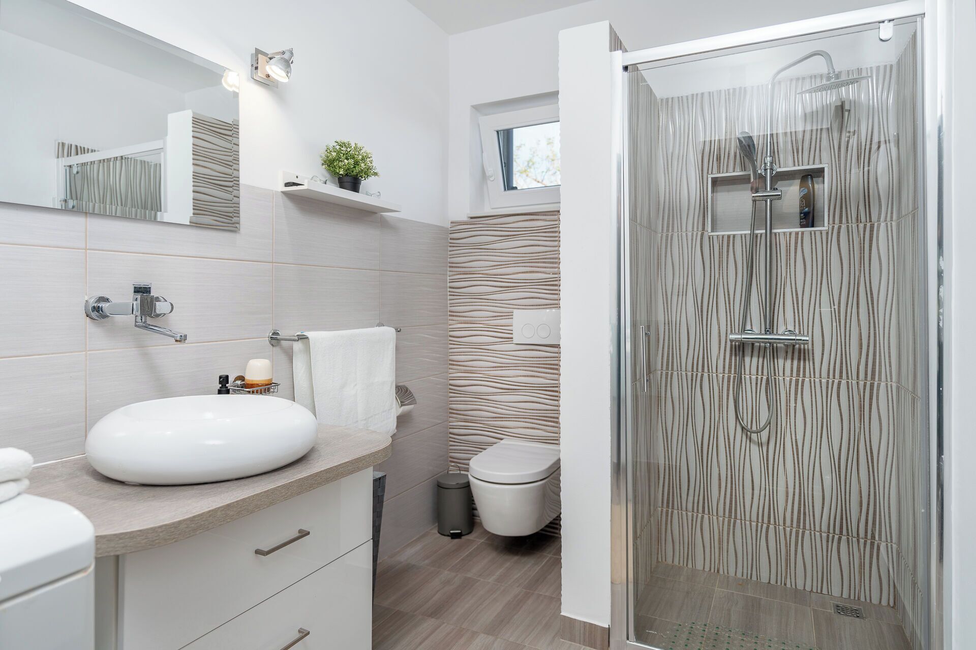 A modern bathroom with a glass-enclosed shower, a white sink, and a mirror above the sink.