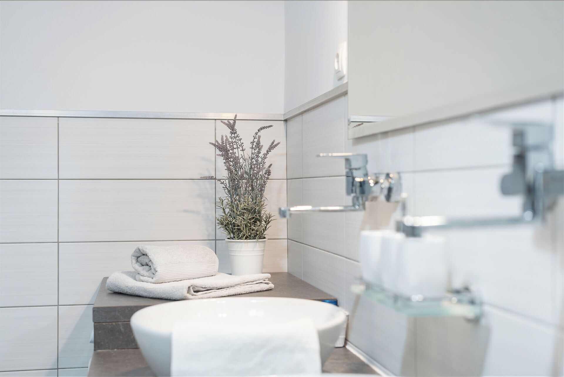 A modern bathroom with a white tiled wall, a potted plant, a towel, and a glass shower enclosure.